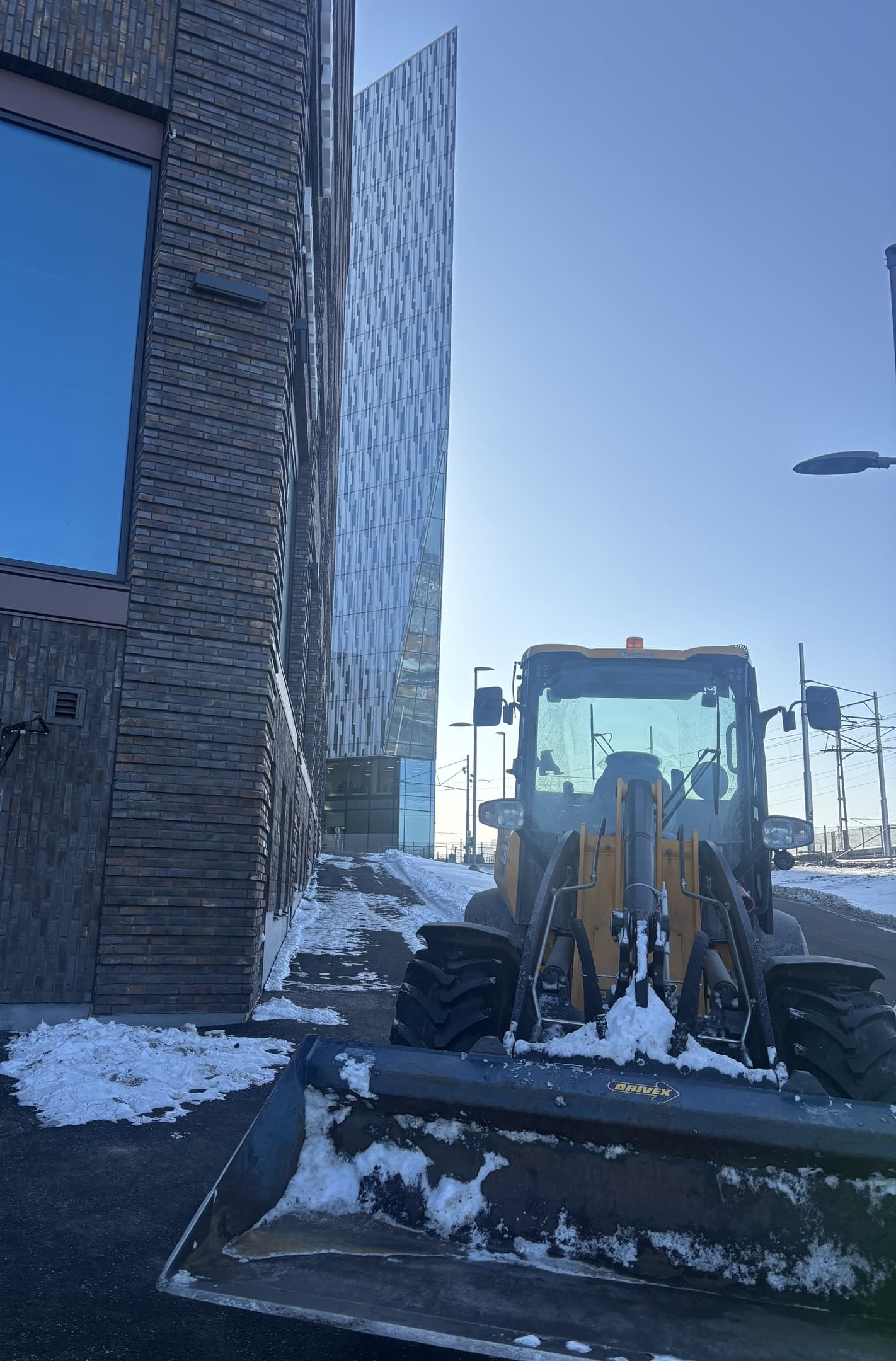 Hjullastare med skopa uppställd vid en fastighet i vinterväder.