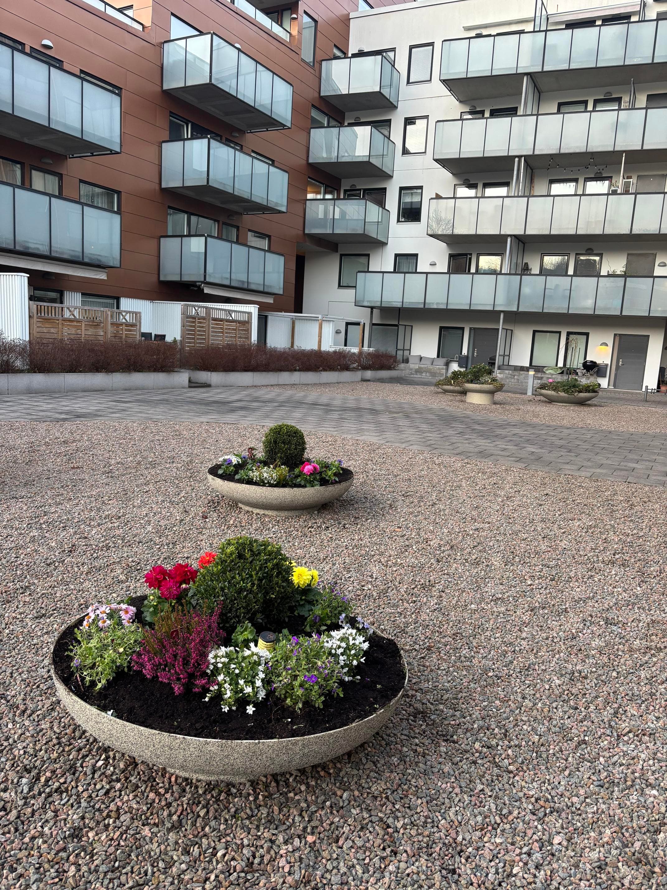 Skött innergård med grusytor, blomsterurnor och flerbostadshus i bakgrunden.