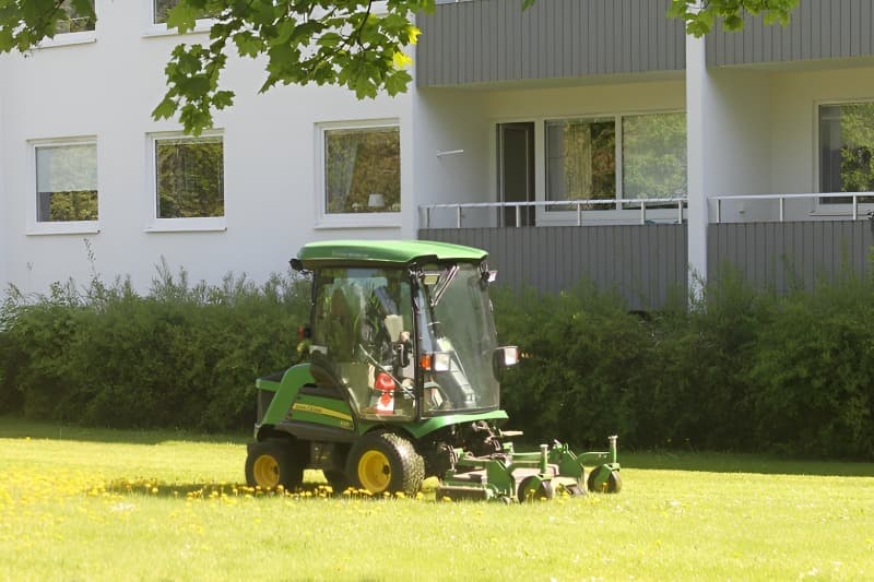 Åkgräsklippare klipper en gräsyta vid en fastighet under sommarhalvåret.